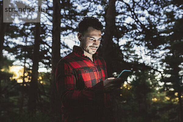 Mann benutzt Smartphone im Wald stehend