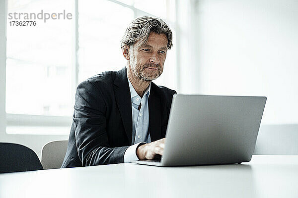 Männlicher Berufstätiger  der einen Laptop benutzt  während er im Büro am Schreibtisch sitzt