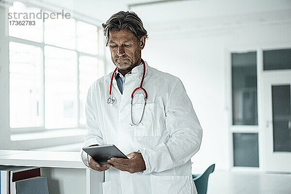 Älterer männlicher Arzt  der ein digitales Tablet im Krankenhaus benutzt