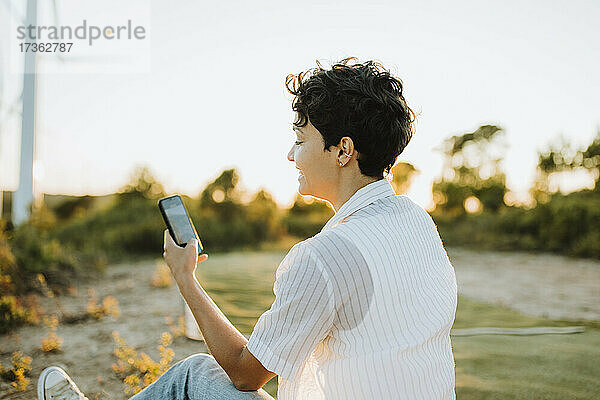 Frau mit kurzen Haaren benutzt Smartphone bei Sonnenuntergang