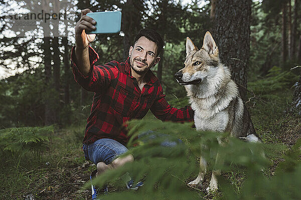 Männlicher Wanderer nimmt Selfie durch Smartphone mit Hund im Wald