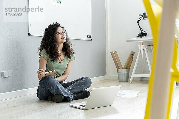 Geschäftsfrau  die mit ihrem Laptop auf dem Boden im Büro sitzt und nachdenkt