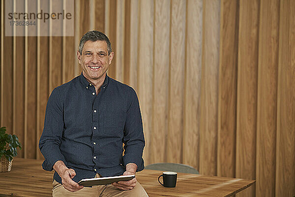 Geschäftsmann lächelt  während er mit einem Tablet auf einem Konferenztisch im Sitzungssaal sitzt