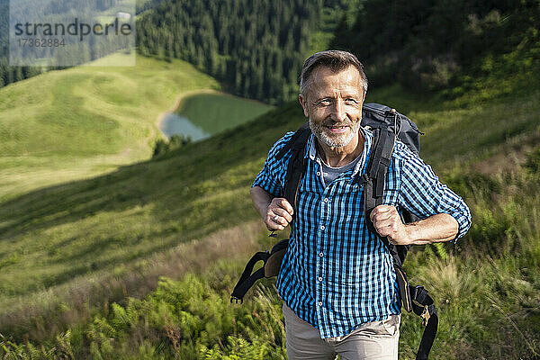 Lächelnder männlicher Rucksacktourist beim Wandern auf einem Berg
