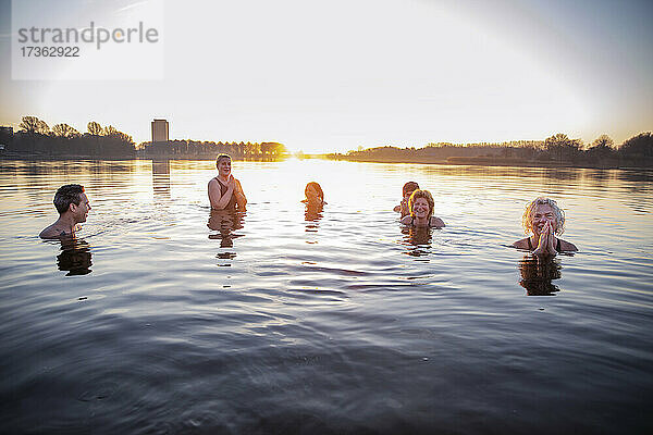 Lächelnde Frauen meditieren  während sie mit männlichen Freunden im Wasser Spaß haben