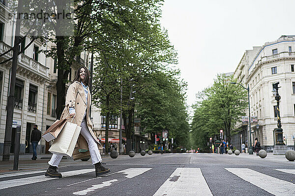 Junge Frau mit Einkaufstüten beim Überqueren der Straße in der Stadt