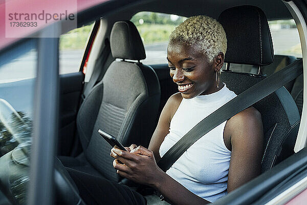 Lächelnde Frau  die ein Mobiltelefon benutzt  während sie im Auto sitzt