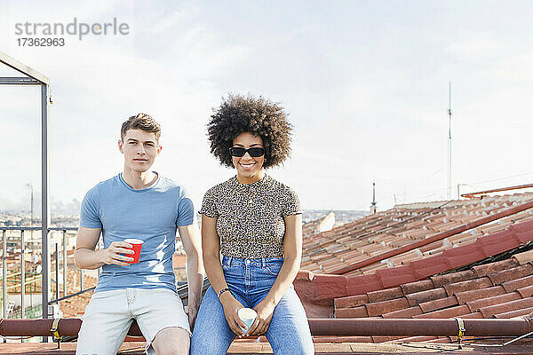 Männliche und weibliche Freunde mit Trinkbechern sitzen zusammen auf der Terrasse