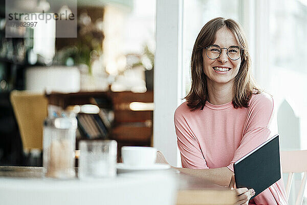 Glückliche junge Geschäftsfrau sitzt mit digitalem Tablet in einem Cafe