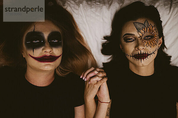 Freundinnen mit bösem Make-up halten sich auf dem Bett liegend an den Händen