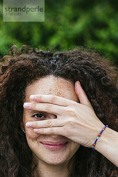 Lächelnde Frau mit lockigem Haar  die durch die Finger schaut