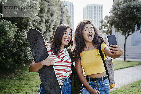 Junge Frau nimmt Selfie durch Smartphone mit weiblichen Freund hält Skateboard im Park