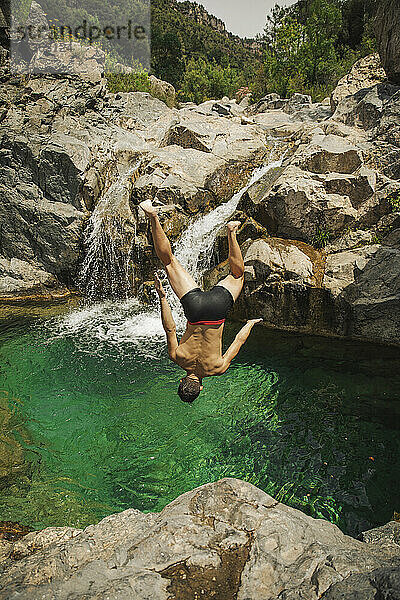 Mann ohne Hemd springt an einem sonnigen Tag in einen Wasserfall