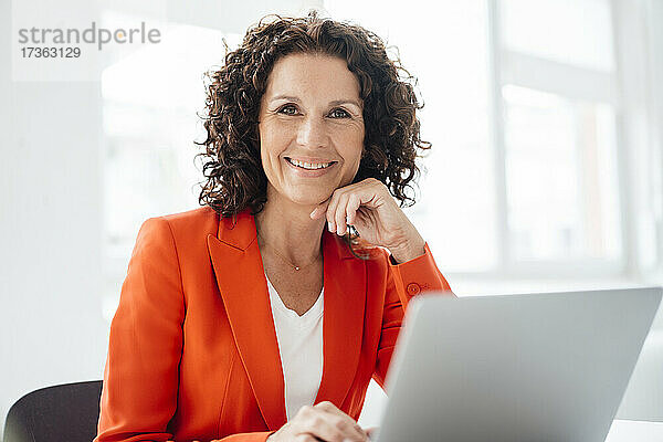 Lächelnde Geschäftsfrau mit Laptop im Büro sitzend