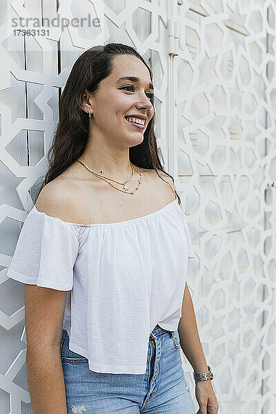 Lächelnde schöne junge Frau vor einer Wand stehend