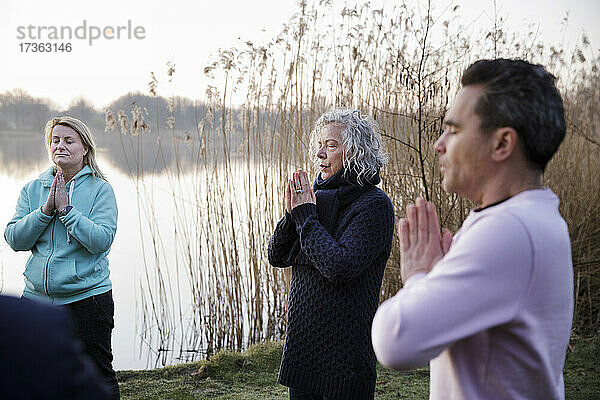 Älterer Mann meditiert mit Frauen am Wasser