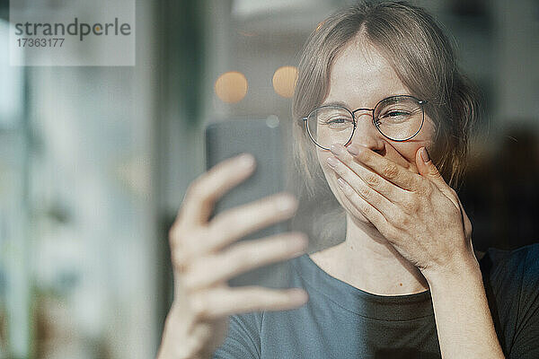 Weibliche Fachkraft bedeckt den Mund während eines Videoanrufs über ein Mobiltelefon