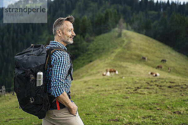 Lächelnder männlicher Wanderer mit der Hand in der Tasche beim Wandern auf einem Berg