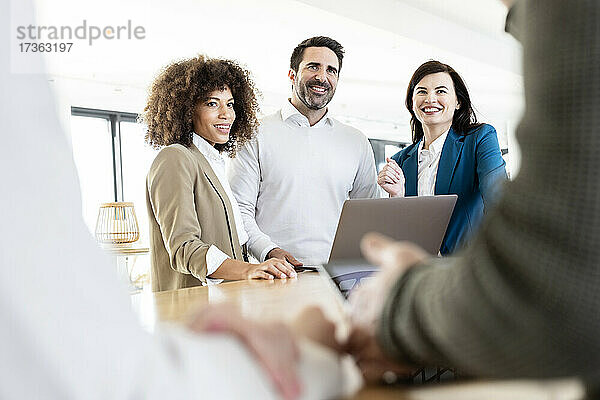Lächelnde männliche und weibliche Fachleute  die einen Kollegen bei einer Besprechung im Büro betrachten