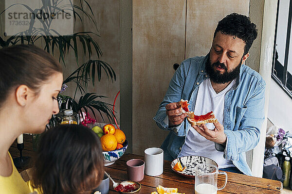Mann isst Essen  während er mit seiner Familie am Tisch sitzt