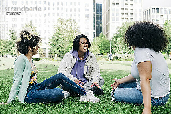 Junger Mann im Gespräch mit multiethnischen Freundinnen im Park