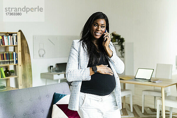 Lächelnde schwangere Berufstätige  die zu Hause mit ihrem Handy telefoniert