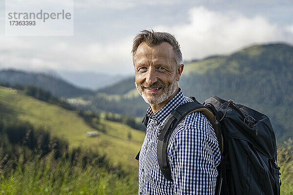 Lächelnder männlicher Wanderer mit Rucksack auf einem Berg