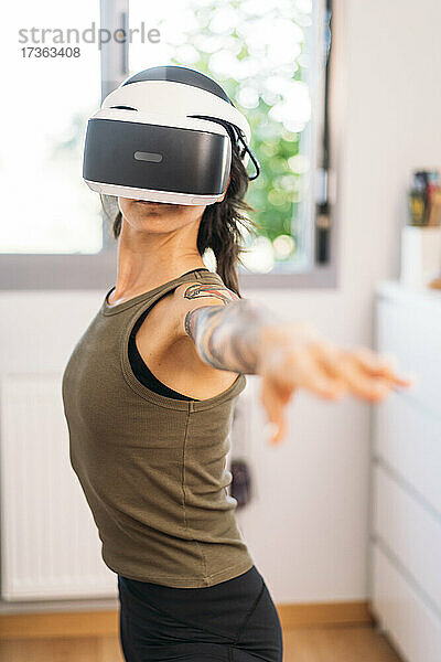 Eine Frau im mittleren Erwachsenenalter benutzt ein Virtual-Reality-Headset  während sie zu Hause trainiert