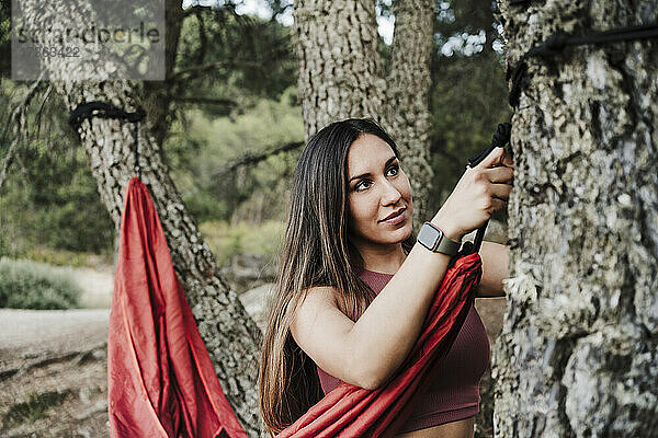 Frau bindet Seil der Hängematte an Baum im Wald