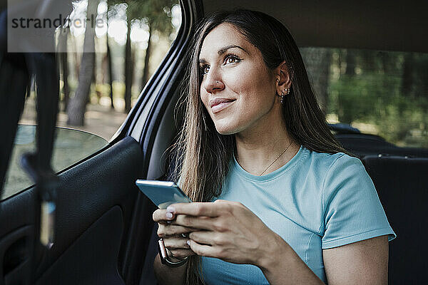 Junge Frau mit Handy in der Hand im Auto sitzend
