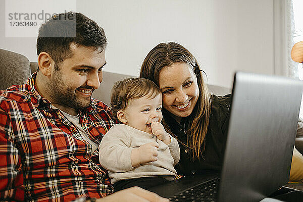 Glückliche Mutter und Vater mit Sohn während eines Videogesprächs auf dem Laptop im Wohnzimmer sitzend