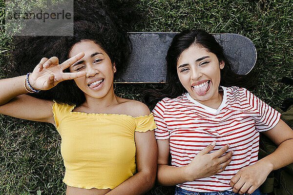 Fröhliche junge Frauen strecken die Zunge heraus  während sie im Park liegen