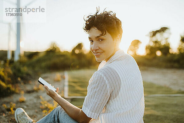 Lächelnde Frau mit Mobiltelefon bei Sonnenuntergang