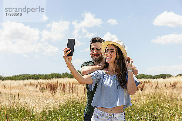 Lächelnde Frau nimmt Selfie mit Freund durch Smartphone auf sonnigen Tag