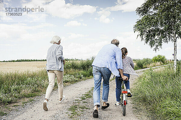 Enkelin fährt Fahrrad  während die Großeltern auf einem unbefestigten Weg laufen