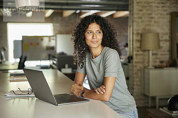 Nachdenkliche Geschäftsfrau  die mit ihrem Laptop am Arbeitsplatz sitzt und wegschaut