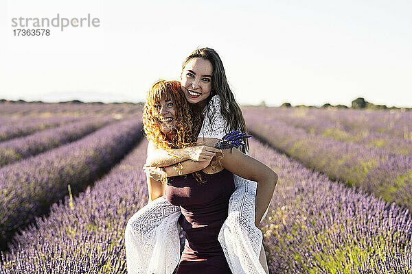 Glückliche Frau nimmt ihre Freundin im Lavendelfeld huckepack