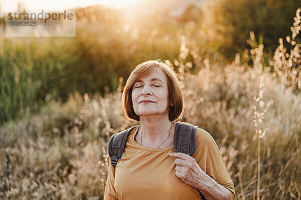 Ältere Frau mit geschlossenen Augen beim Wandern bei Sonnenuntergang