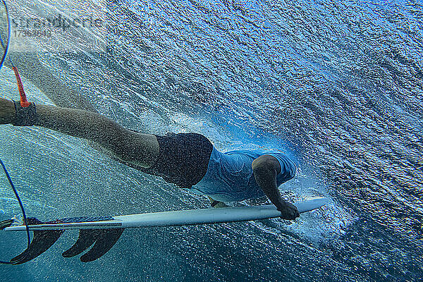 Unterwasseransicht eines jungen Mannes beim Surfen im blauen Wasser des Süd Male Atolls