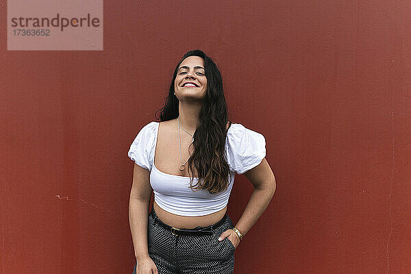 Lächelnde junge Frau vor brauner Wand stehend