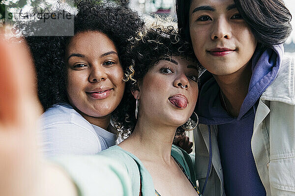 Junge Frau streckt die Zunge heraus  während sie ein Selfie mit multiethnischen Freunden macht