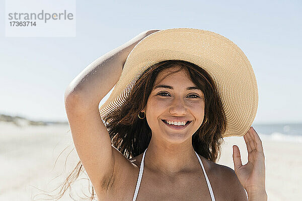 Schöne Frau mit Sonnenhut lächelt  während sie am Strand genießt