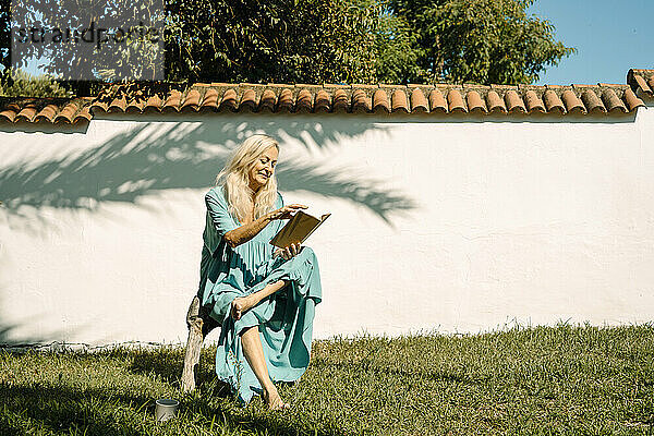 Frau liest ein Buch  während sie an einem sonnigen Tag im Hinterhof sitzt