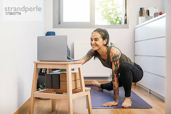 Lächelnde Frau  die zu Hause mit ihrem Laptop online Yoga übt