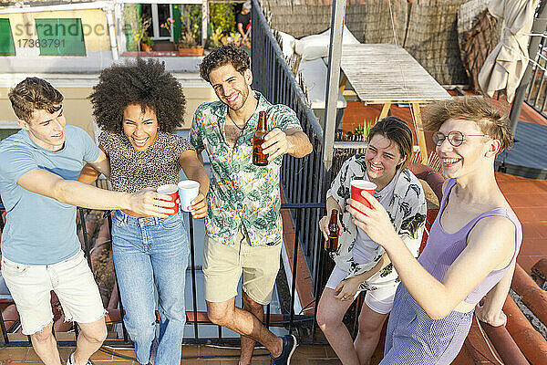 Fröhliche multiethnische männliche und weibliche Freunde stoßen während einer Party auf dem Dach mit Getränken an