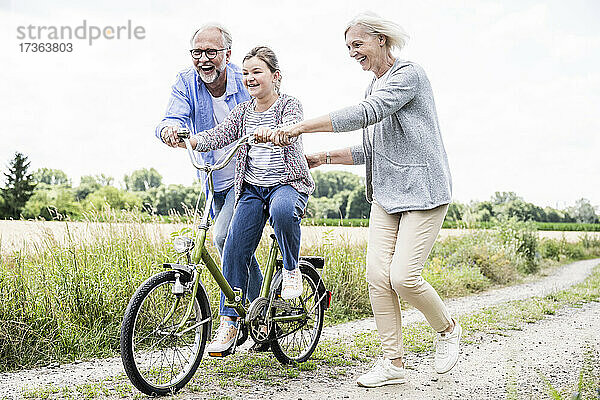 Älterer Mann und Frau  die einem Mädchen beim Fahrradfahren auf einem Feldweg helfen