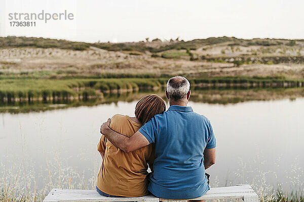 Mutter ruht mit dem Kopf auf der Schulter ihres Sohnes  während sie auf einer Bank in der Nähe des Sees sitzt