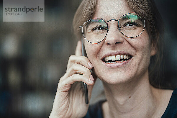 Glückliche junge Geschäftsfrau mit Brille  die mit einem Smartphone telefoniert