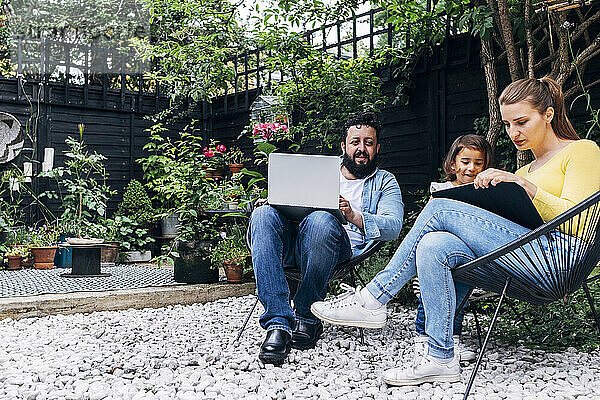 Mann mit Laptop sitzt bei einer Frau  die ein Mädchen im Hinterhof unterrichtet