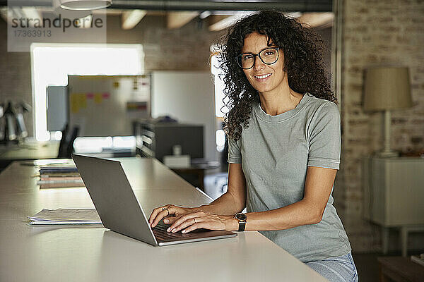 Berufstätige Frau  die am Schreibtisch sitzend einen Laptop benutzt